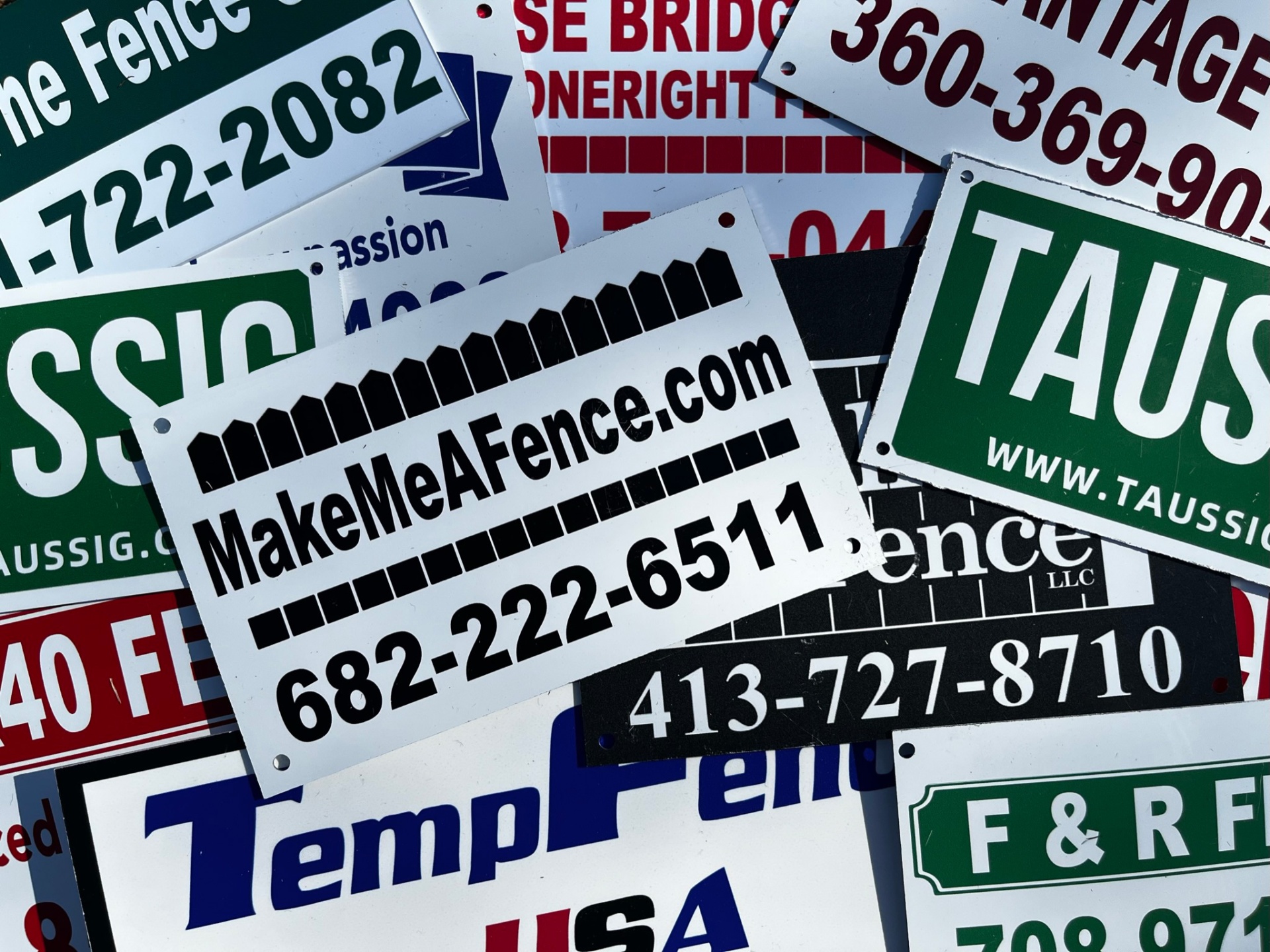 Stack of finished custom fence signs in red, green, blue and black showing different fencing company brands and phone numbers